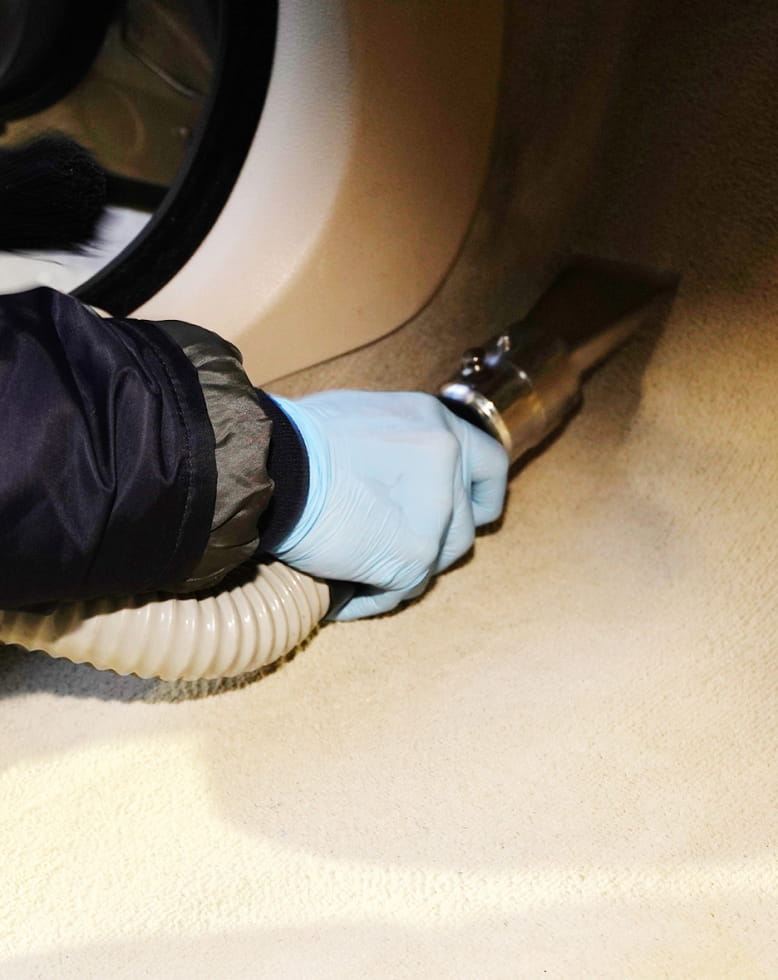 青い手袋をした手が掃除機のノズルで車のカーペットを掃除している様子