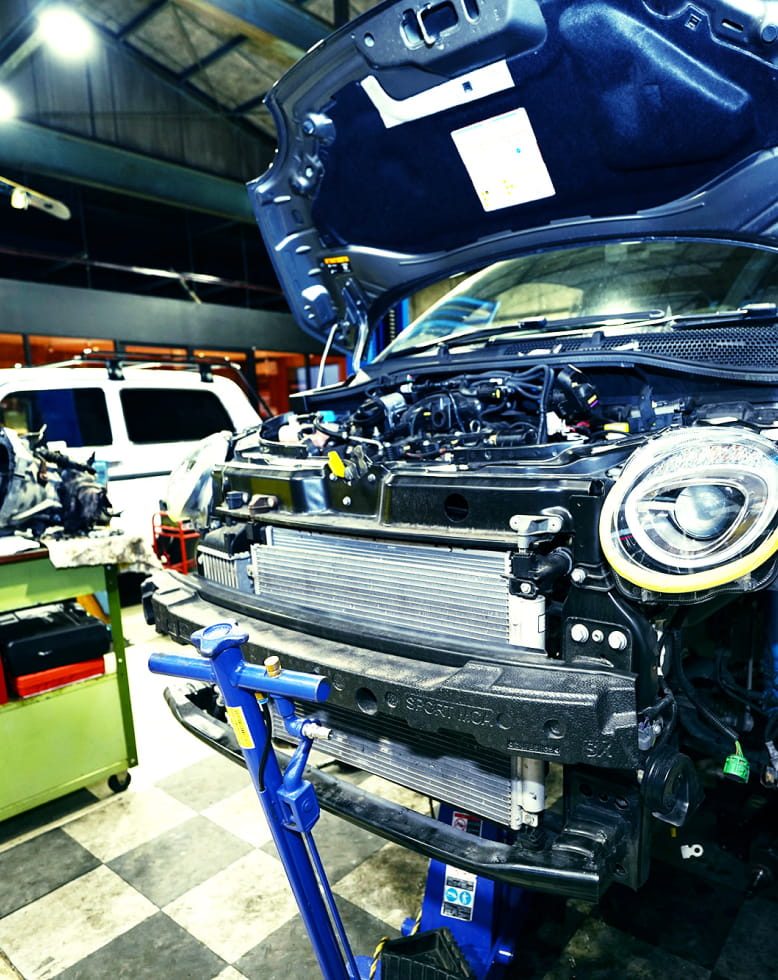 整備工場でボンネットを開けフロントバンパーを外した車のエンジン周りを点検している様子