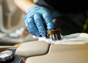 車内のレザーシートをブラシで掃除する青い手袋の手