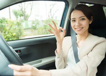 運転席でシートベルトを締め、笑顔でOKサインを出す女性
