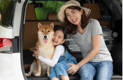 車の荷室に座り笑顔で犬を抱きしめる女の子と隣で寄り添う女性